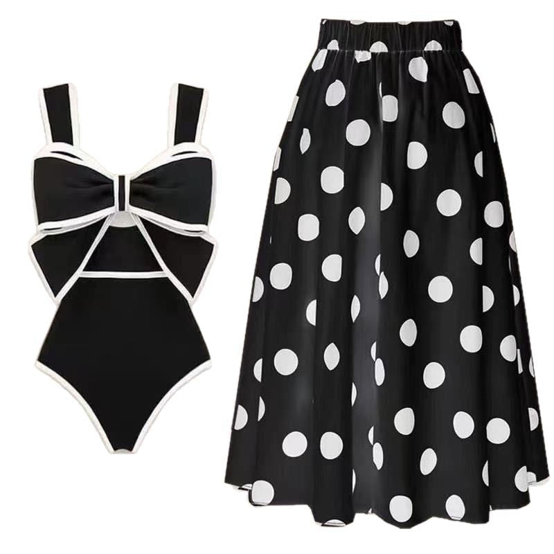 Bikini and skirt set in black and white with polka dots and bow detail, solid background.