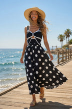Polka dot dress in black and white, sleeveless and flowy, lifestyle shot with sun hat.