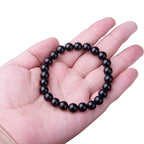Black onyx bracelet held in hand, featuring smooth finish on white background
