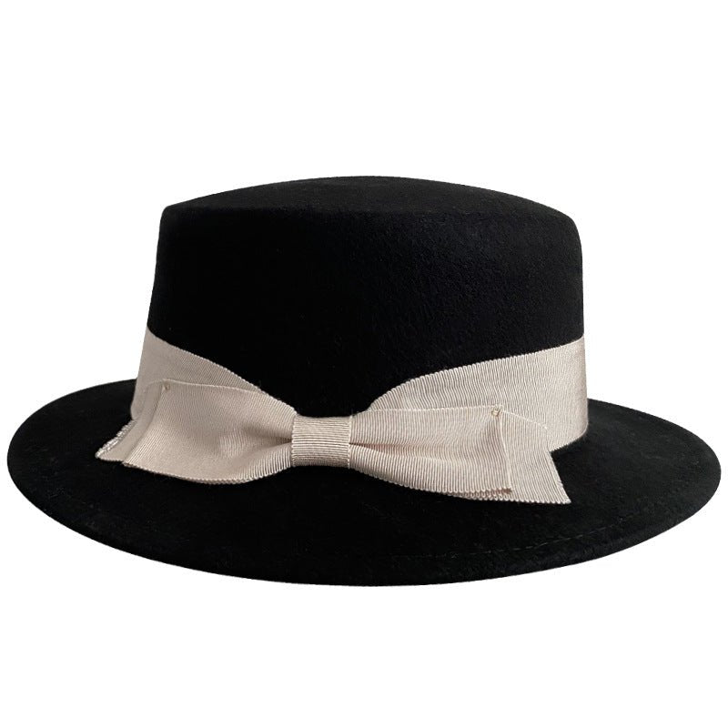 Detail shot of a black bow flat-brimmed cap, highlighting the bow detail on a white background.