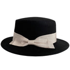 Detail shot of a black bow flat-brimmed cap, highlighting the bow detail on a white background.