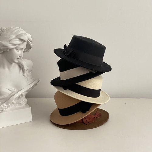 Stack of black and khaki flat-brimmed caps with bow details, showcasing various styles in a natural setting.