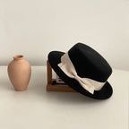 Black flat-brimmed cap featuring a bow detail, elegantly displayed against a natural background.