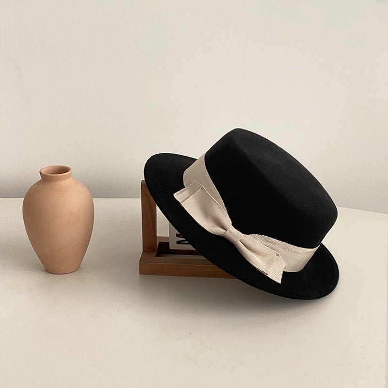 Black flat-brimmed cap featuring a bow detail, elegantly displayed against a natural background.