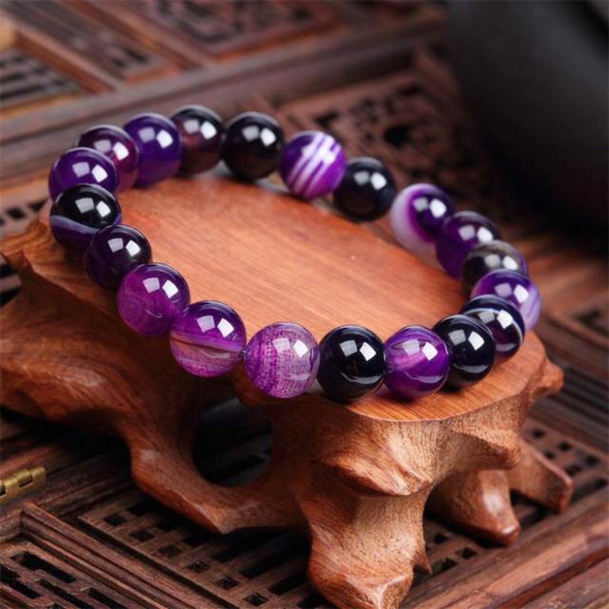 Lifestyle shot of Violet Agate Bracelet in a natural setting, featuring round beads in purple and black tones.