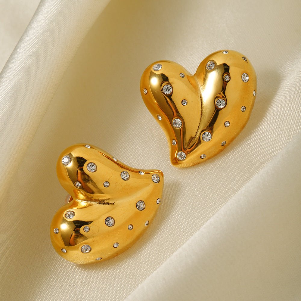 Detail close-up of gold heart earrings with shiny finish and inlaid diamonds, elegant design.