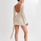 Back view of the white backless long-sleeved dress showcasing the slim fit and V-shaped back detail.