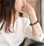 Lifestyle shot of a woman wearing Gold Sapphire Bracelet, featuring round beads in black and gold colors in a casual setting.