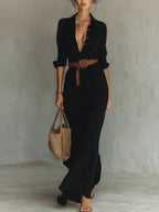 Lifestyle shot of a black long dress with a belted waist and button lapel, showcasing elegant minimalist style.