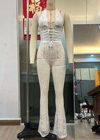 Front view of a white lace-up jumpsuit highlighting its see-through features and deep V-neck.