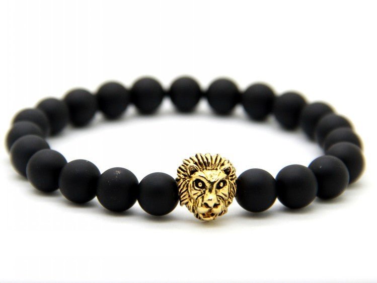 Detail close-up of black stone bracelet with lion charm, featuring gold accents on white background