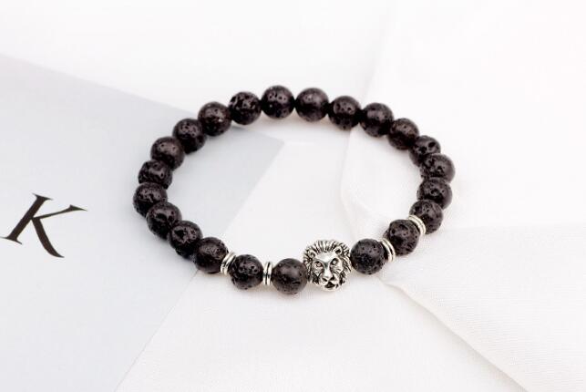 Detail close-up of black stone bracelet with lion head charm, showcasing silver accents on white background