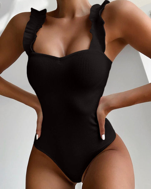Detail of the black one-piece swimsuit showcasing ruffle straps and a push-up design, chic minimalist fashion.