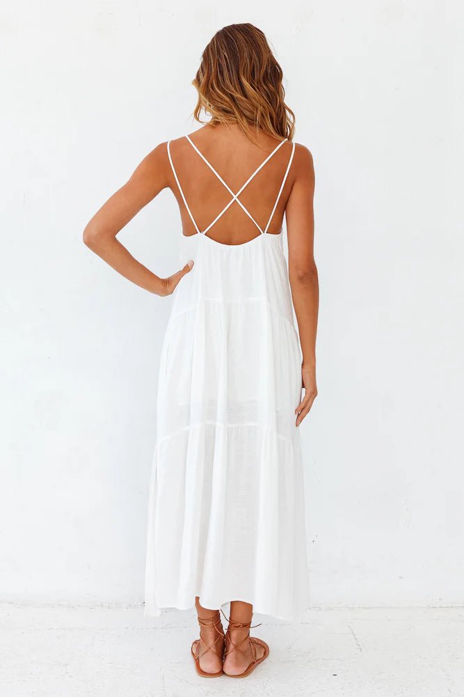 Back view of a white carbell maxi dress with crossed straps, showcasing its flowy fabric against a solid background.