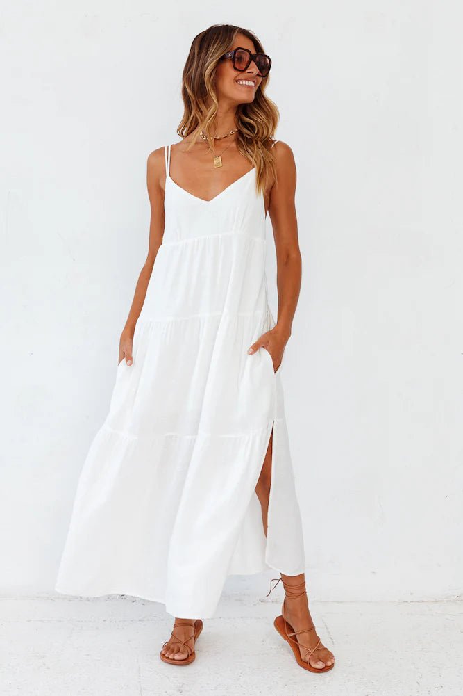 Flowy white carbell maxi dress with spaghetti straps, lifestyle shot against a solid background.