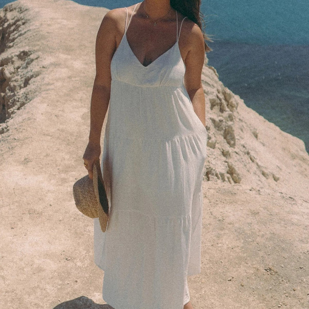 Chic white maxi dress with flowy fabric and spaghetti straps, styled in a natural setting.