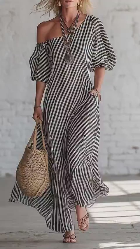 Lifestyle shot of a gray and beige striped off-shoulder maxi dress, flowy fabric in a natural setting.