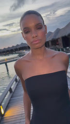 Woman in a black strapless jumpsuit, elegant minimalist style in an outdoor setting.