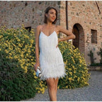 Chic white A-line mini dress with tassels and sequins, styled in a natural setting.