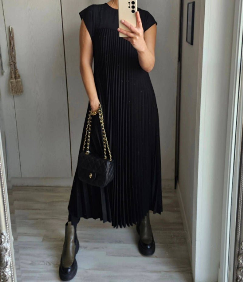 Black pleated long dress with cap sleeves, highlighting minimalist elegance in a studio setting.