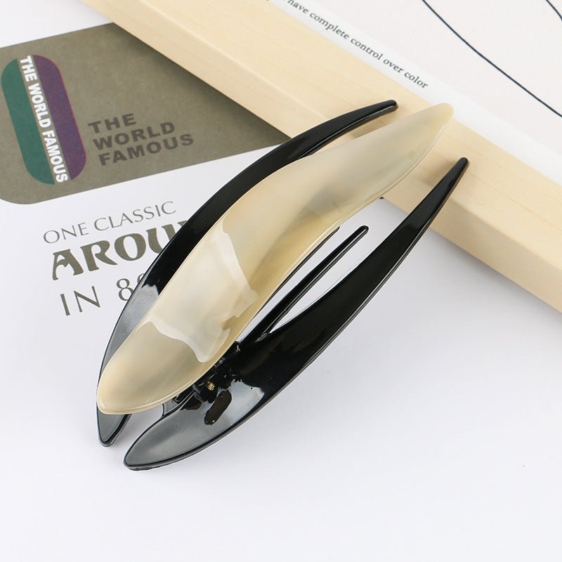 Detail close-up of a sleek acetate hairpin in cream and black, showcasing its elegant curves.
