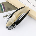 Detail close-up of a sleek acetate hairpin in cream and black, showcasing its elegant curves.