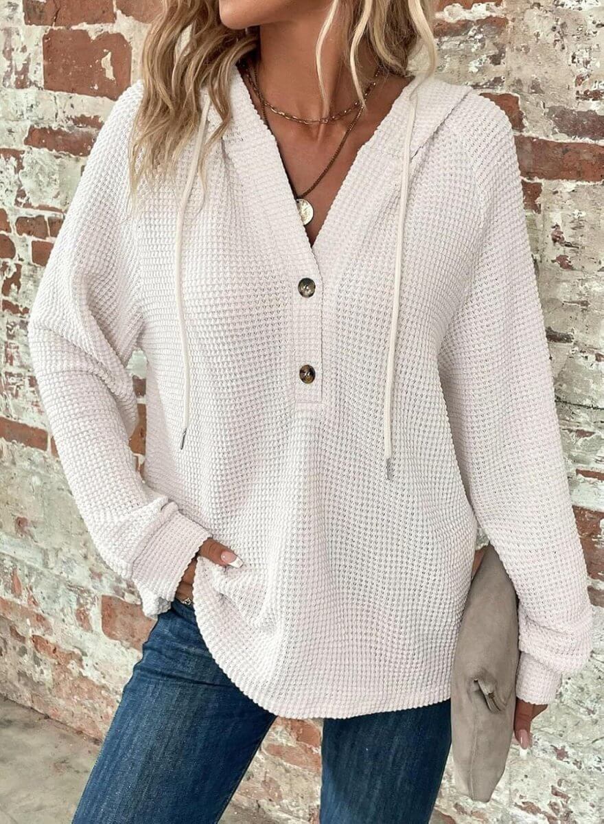 Lifestyle shot of a woman in a white waffle hooded pullover sweater featuring a button closure.