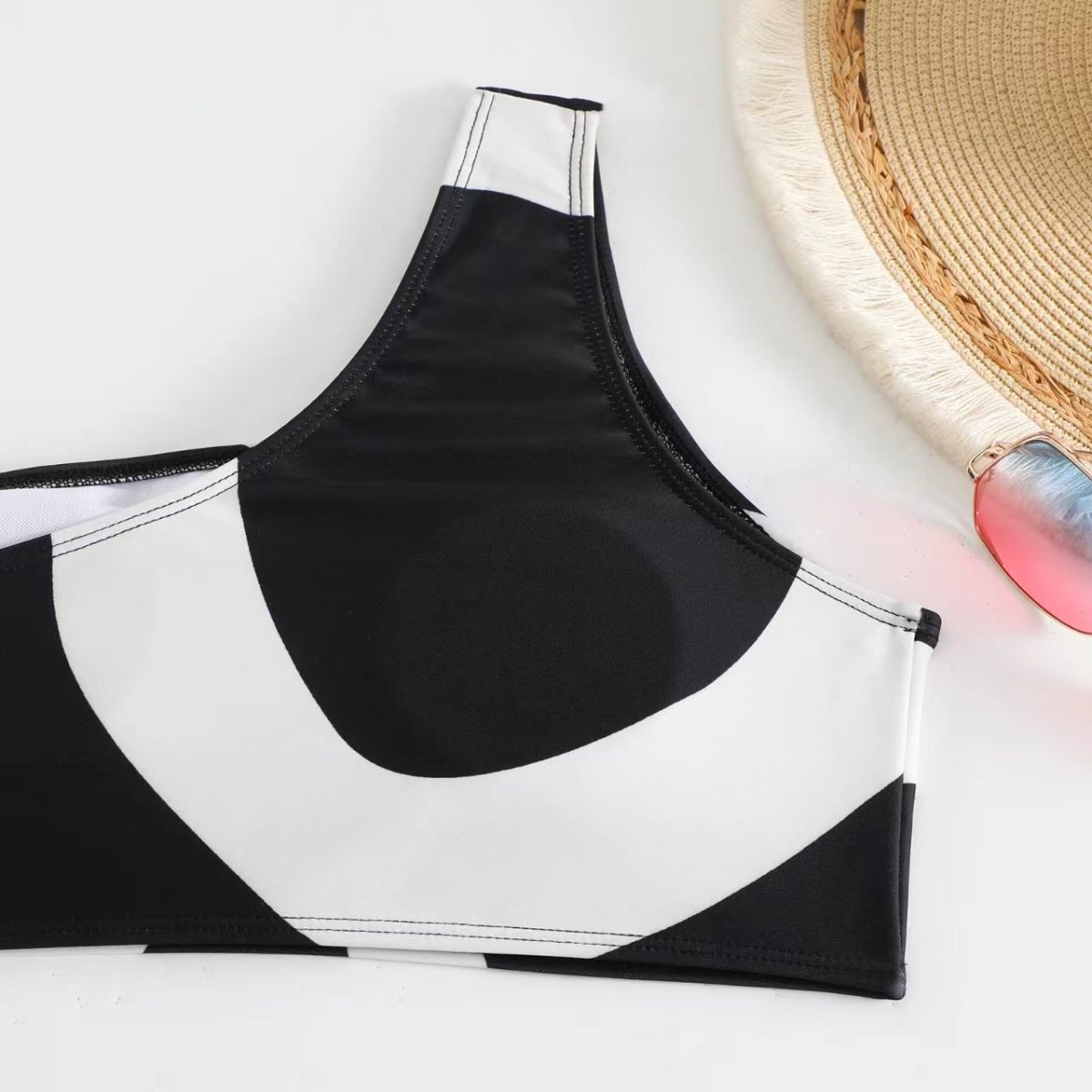 Detail view of black bikini top with one-shoulder design, highlighting textured fabric.