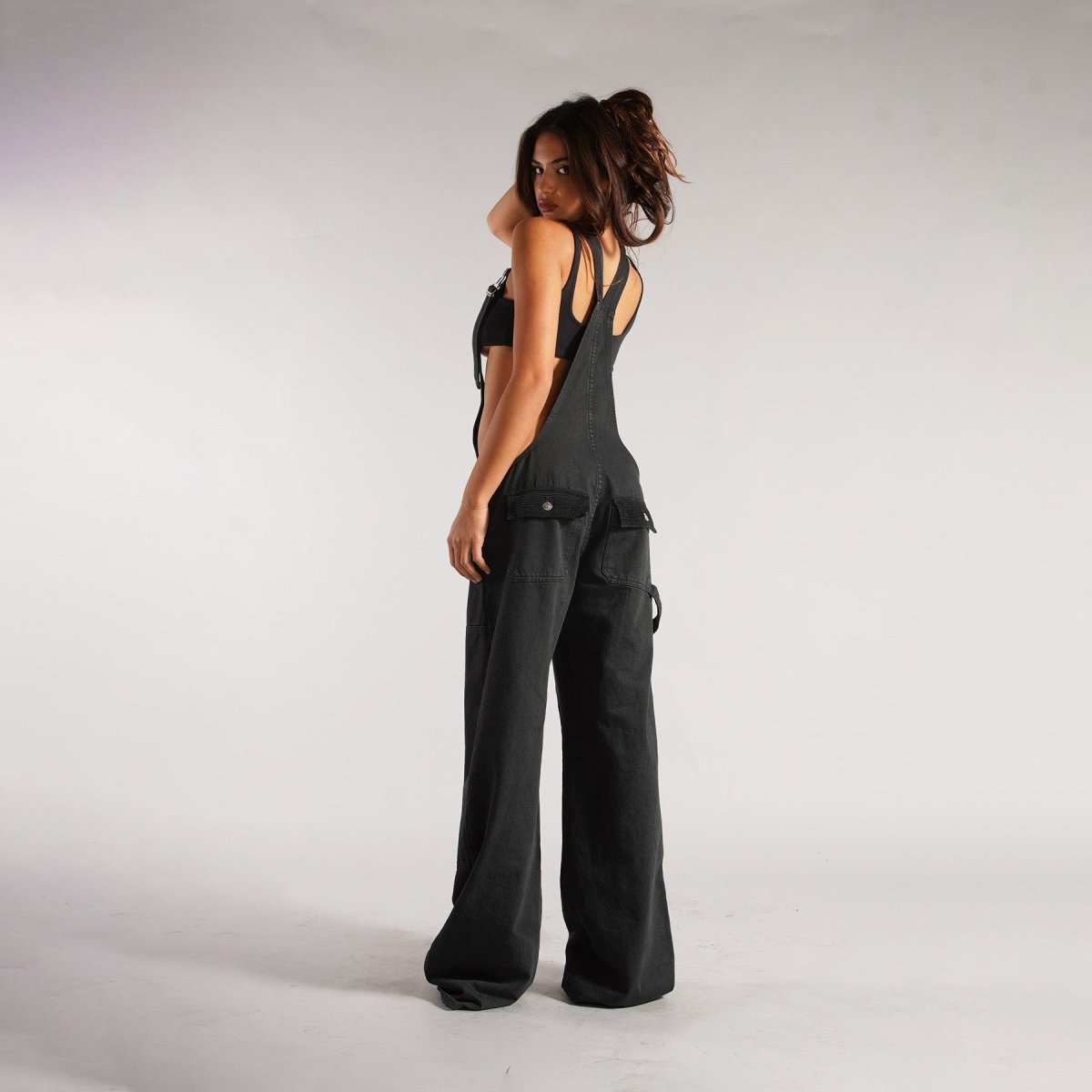 Back view of black loose denim overalls emphasizing the high waist design and wide leg cut, a trendy addition to any wardr…