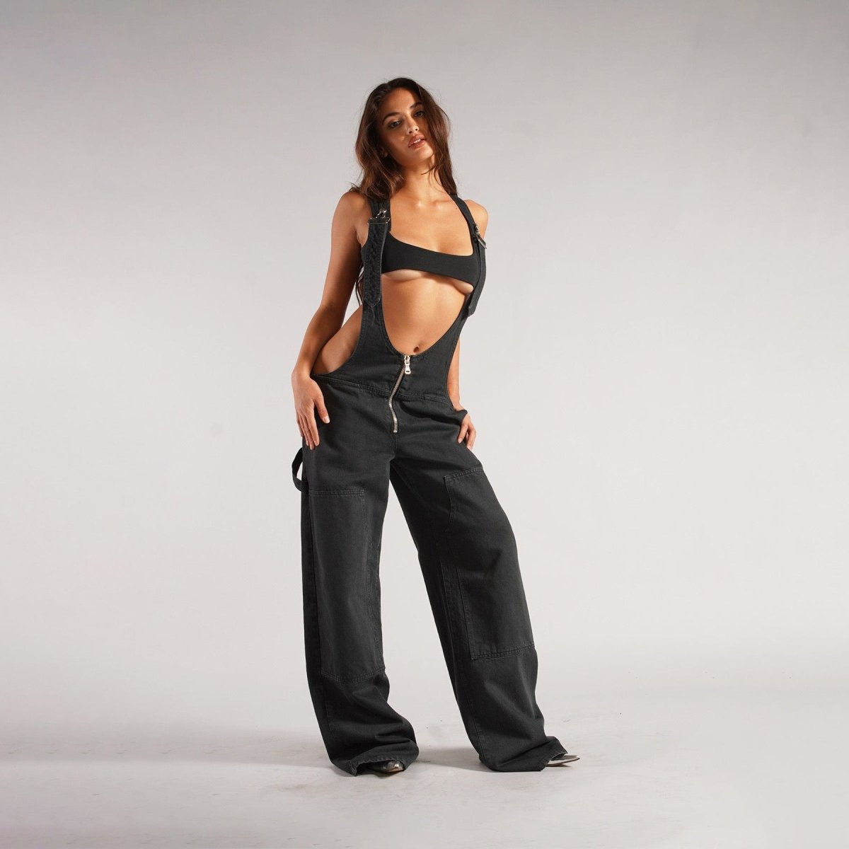 Detailed view of black loose denim overalls with high waist and wide leg features, highlighting the unique zipper pockets.